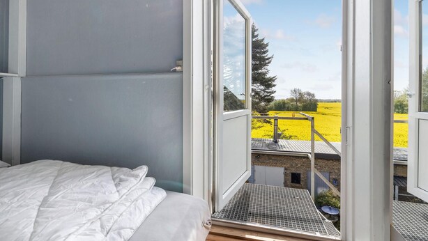 A bedroom with a large window, a bed, and a view of a field.