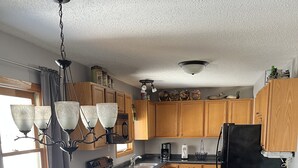 A kitchen with wooden cabinets, a black refrigerator, a dining table with chairs, and a chandelier. - Up North, Outdoor Enthusiast’s Paradise! (Birchwood)