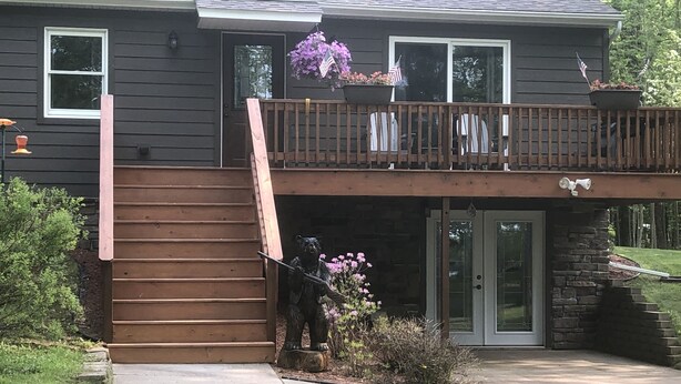 A two-story house with a wooden deck, a front porch, and a statue of a bear. - Up North, Outdoor Enthusiast’s Paradise! (Birchwood)