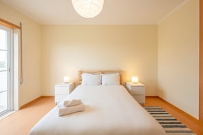 A hotel room with a large bed, two bedside tables with lamps, a window with a view, and a striped rug.