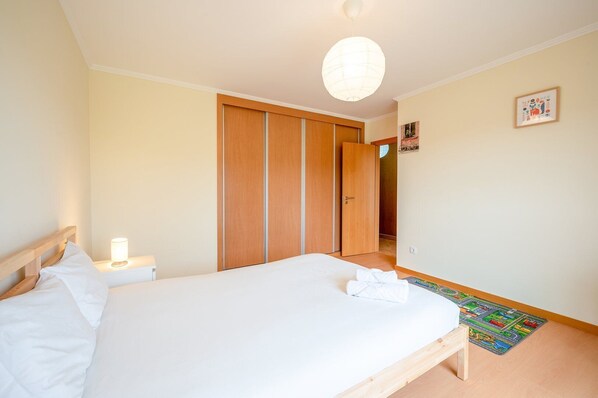 A bedroom with a bed, bedside lamp, wooden wardrobe, and a colorful rug.