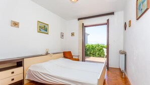 Ein Schlafzimmer mit Bett, Schreibtisch und Stuhl. An den Wänden hängen Bilder und es gibt einen Blick ins Freie.