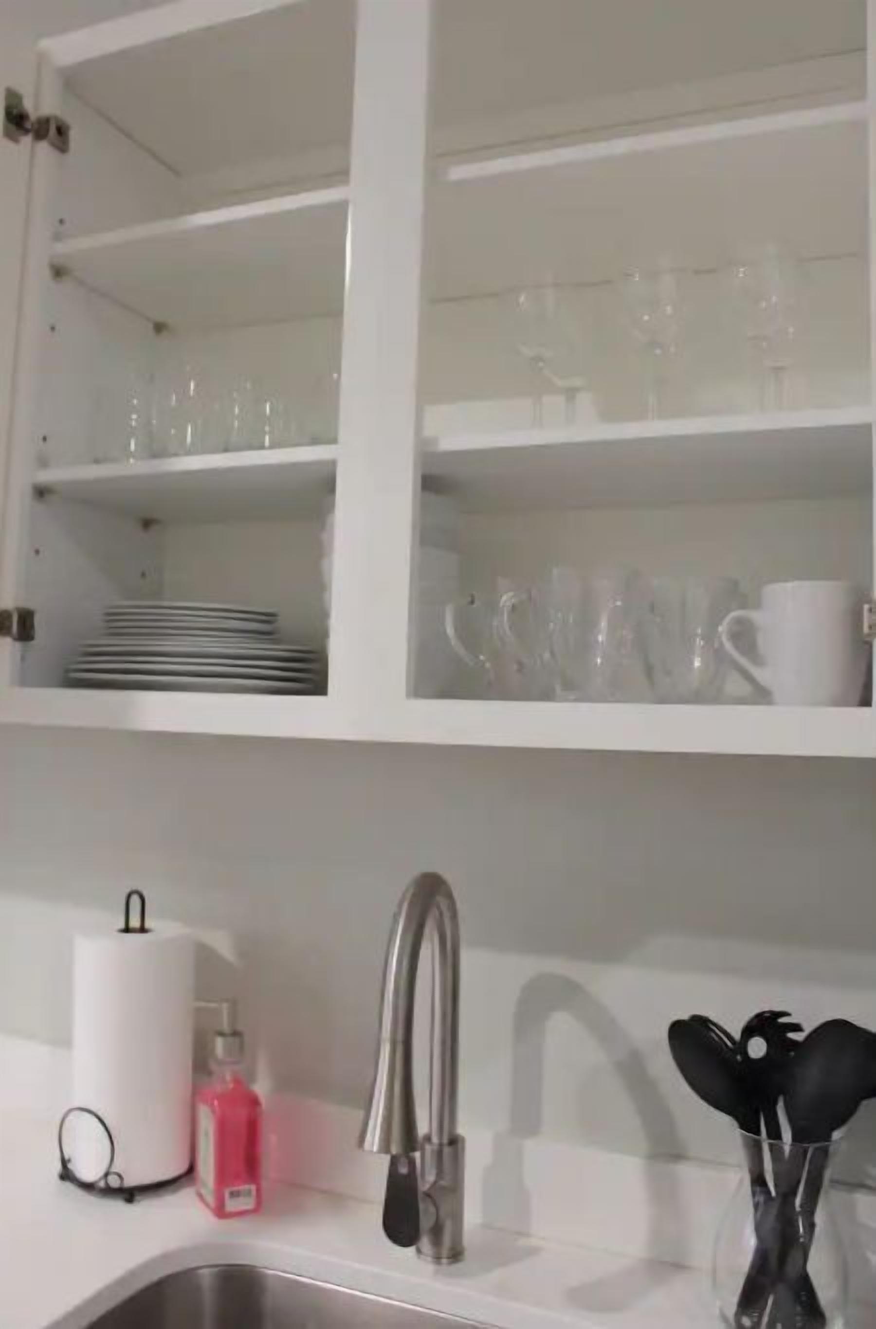 A kitchen with white cabinets, a stainless steel sink, and a glass vase with utensils.