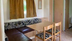 A room with a wooden table, two chairs, a bench with floral upholstery, a mirror, and a door. - Mobile home in Xaintrie (SAINT-GENIEZ-Ô-MERLE)