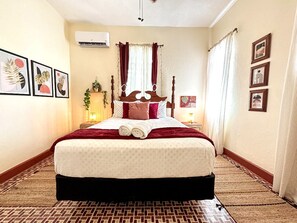 Habitación de hotel con una cama grande, una mesita de noche, aire acondicionado instalado en la pared y cuadros enmarcados en las paredes.