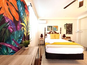 Un dormitorio con cama, mesita de noche, lámpara, una obra de arte en la pared y una planta.