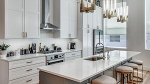 A modern kitchen with white cabinetry, a central island with stools, stainless steel appliances, and pendant lighting. - 2912 Raleigh (Dallas)