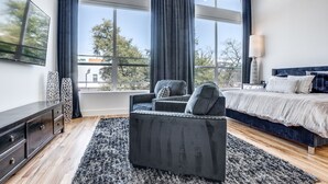 A modern bedroom with a large bed, a dark sofa, and a TV on the wall. - 2912 Raleigh (Dallas)