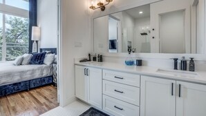A modern bathroom with a large mirror, white cabinets, and a bedside table with a lamp. - 2912 Raleigh (Dallas)