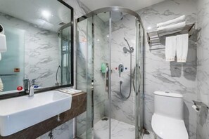 Une salle de bain moderne avec une douche à parois de verre, un mur recouvert de carreaux de marbre, un lavabo blanc et des toilettes.