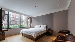 Ein modernes Schlafzimmer mit einem großen Bett, Holzboden, Blick auf Gebäude durch das Fenster und einer Sitzecke mit Ledersesseln.