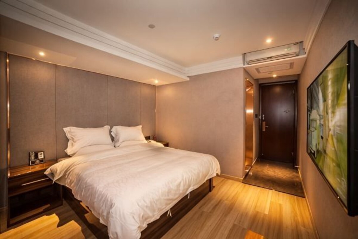 A hotel room with a bed, bedside table, wall-mounted artwork, and a door leading to another room.