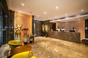 Uma área de recepção de hotel com piso de mármore, balcão de atendimento e espaço para sentar.