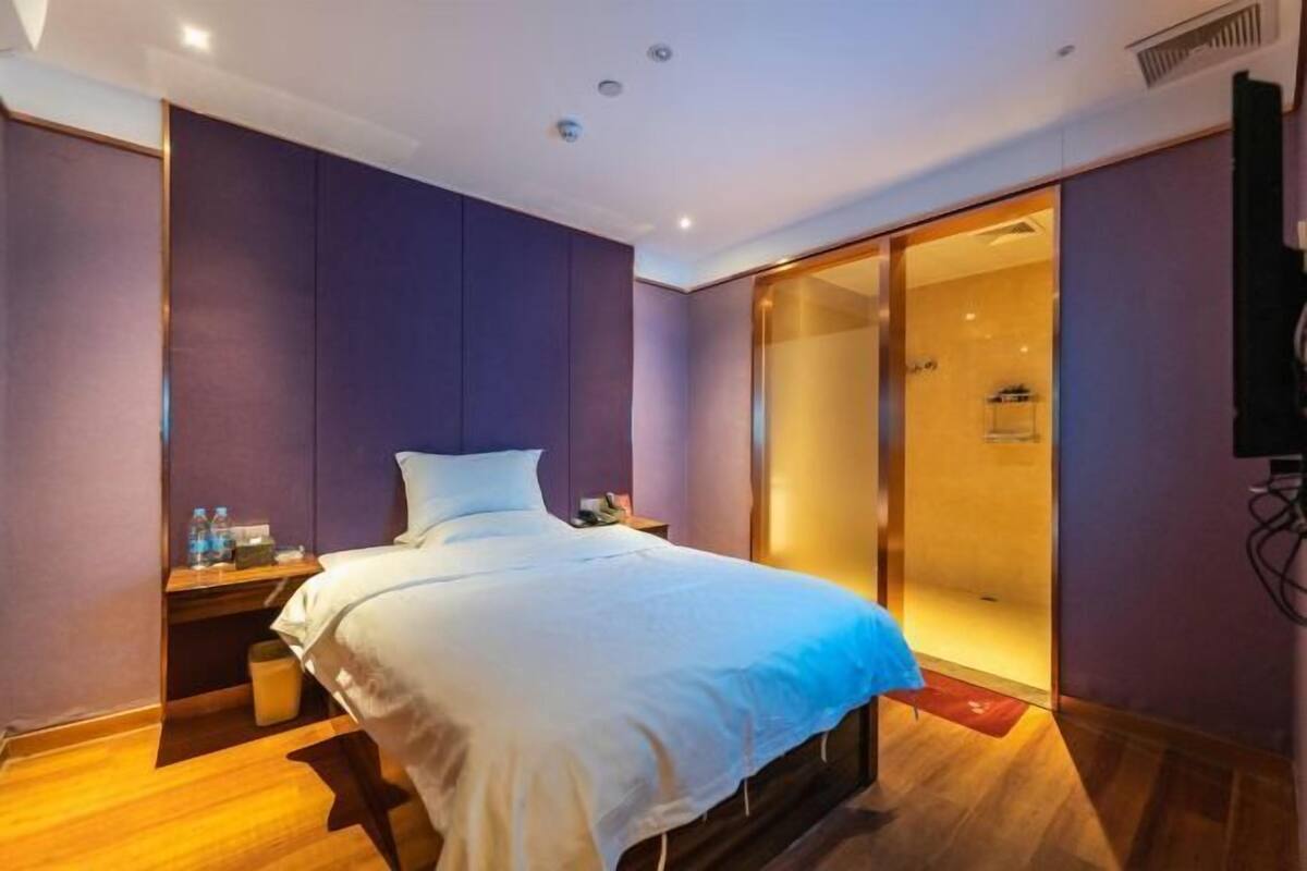 Habitación de hotel con cama, mesita de noche, armario y zona de ducha.