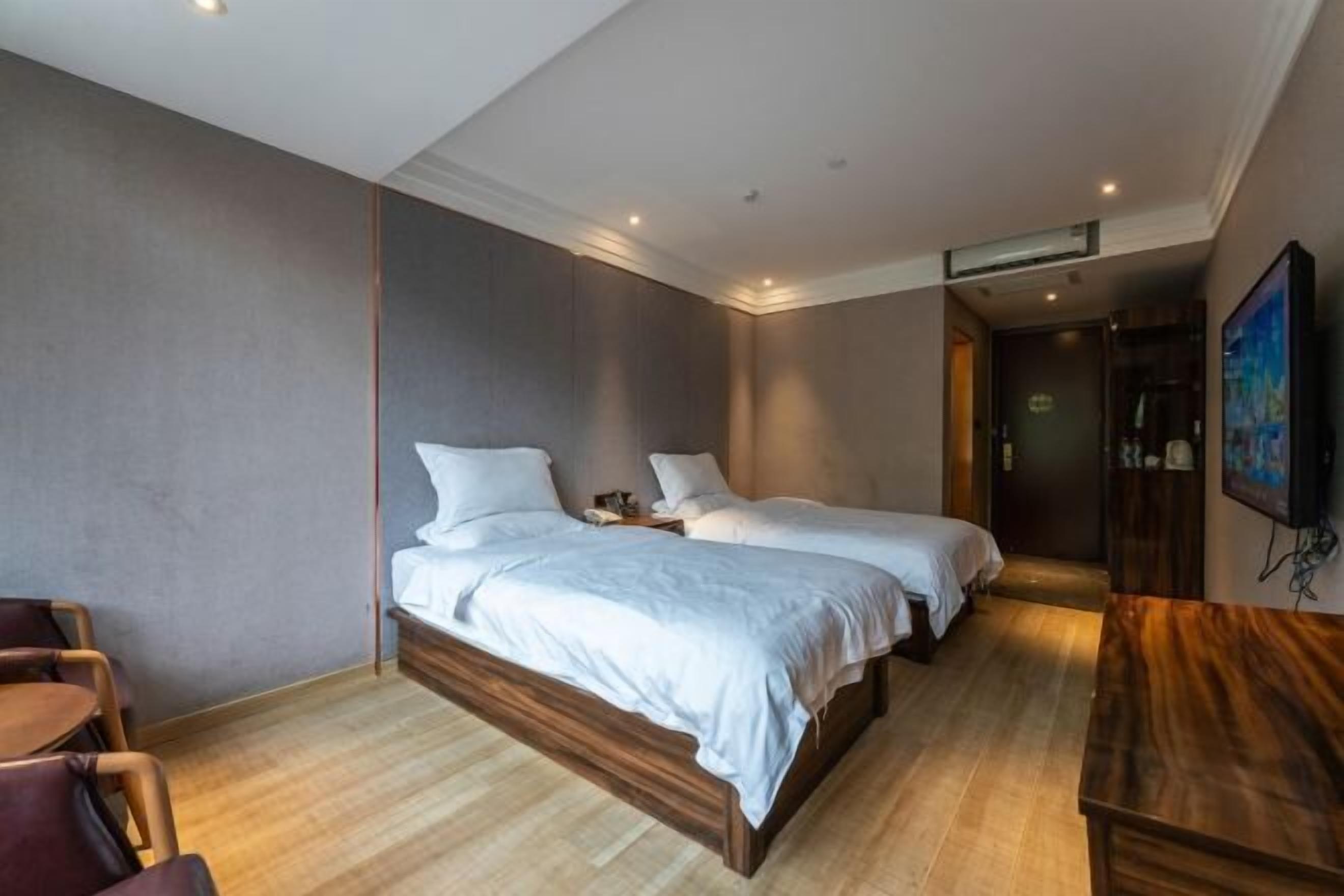 A hotel room with two beds, a wooden desk, a chair, and a TV.