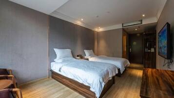 A hotel room with two beds, a wooden desk, a chair, and a TV.