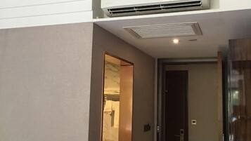 A hotel room with a ceiling-mounted air conditioner, a door leading to another room, and a visible light switch.