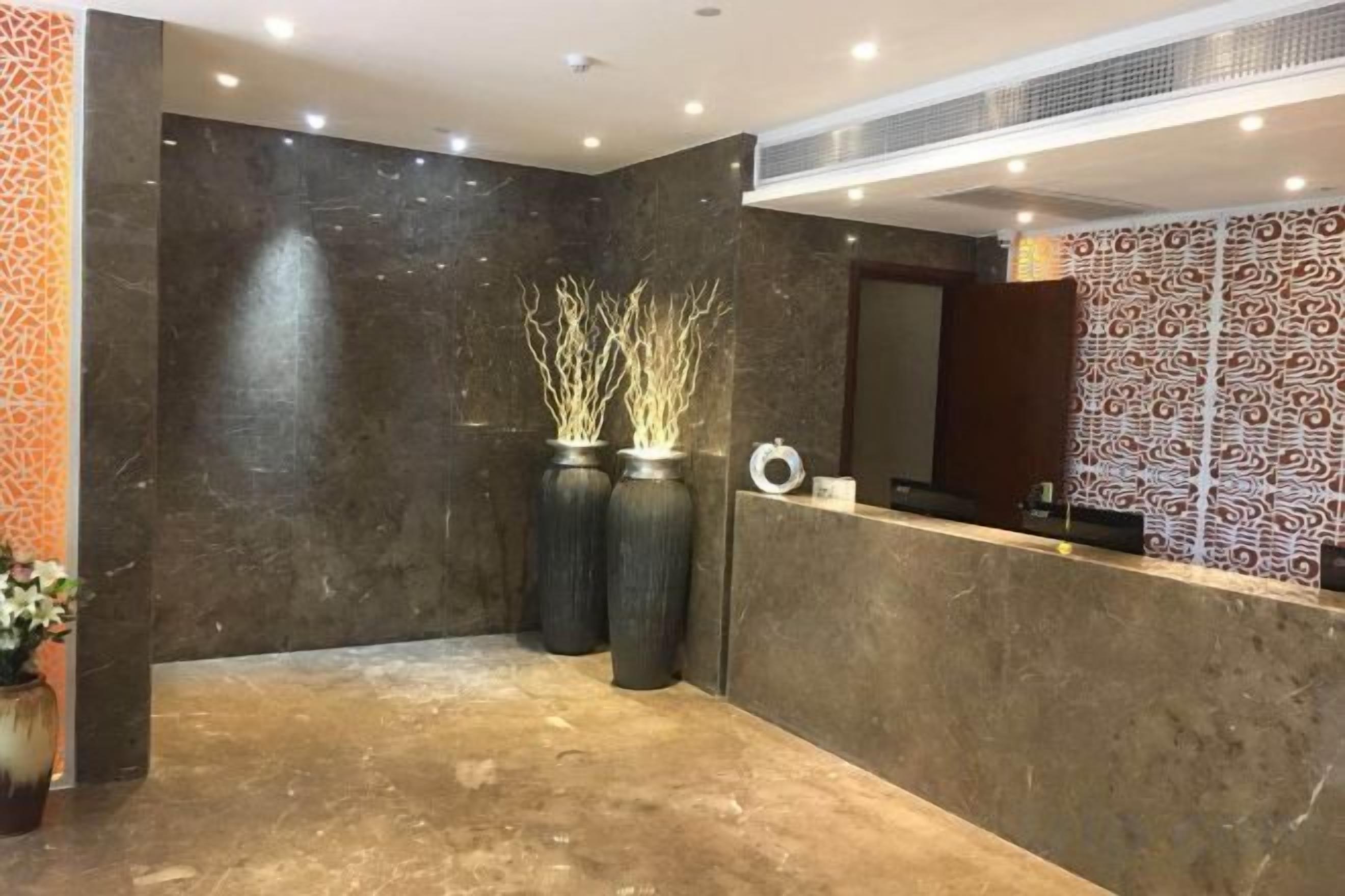 A reception area with a marble floor, two large vases with branches, a reception desk, and patterned wallpaper.