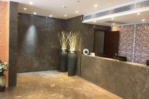 A reception area with a marble floor, two large vases with branches, a reception desk, and patterned wallpaper. - Baba Boutique Hotel (Xiamen)