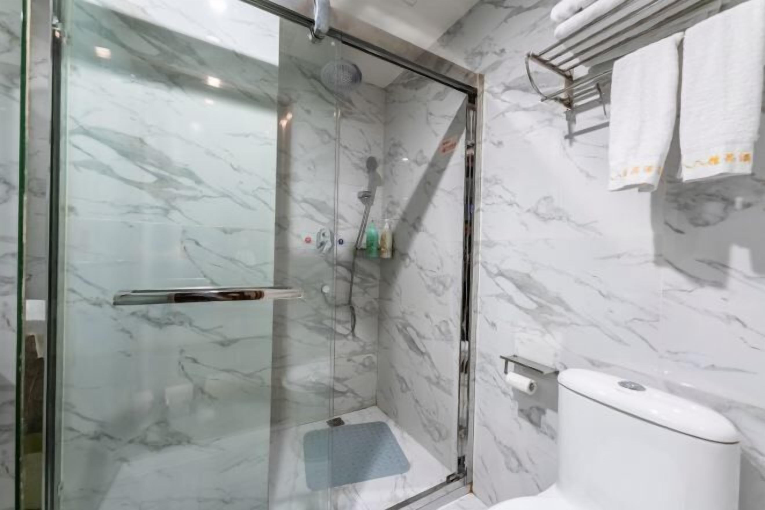 Et moderne badeværelse med et glasafskærmet brusebad, marmorvægge og toilet med papirhåndklædeholder.