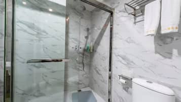 Et moderne badeværelse med et glasafskærmet brusebad, marmorvægge og toilet med papirhåndklædeholder.