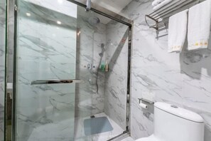 A modern bathroom with a glass-enclosed shower, marble walls, and a toilet with a paper towel holder. - Baba Boutique Hotel (Xiamen)