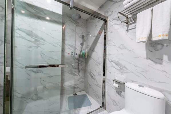 Een moderne badkamer met een douchecabine van glas, marmeren wanden en een toilet met een papieren handdoekhouder.