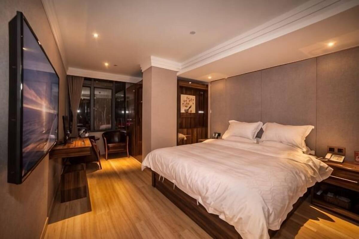 Habitación de hotel con una cama grande, un escritorio con silla, televisión y vista nocturna de la ciudad.