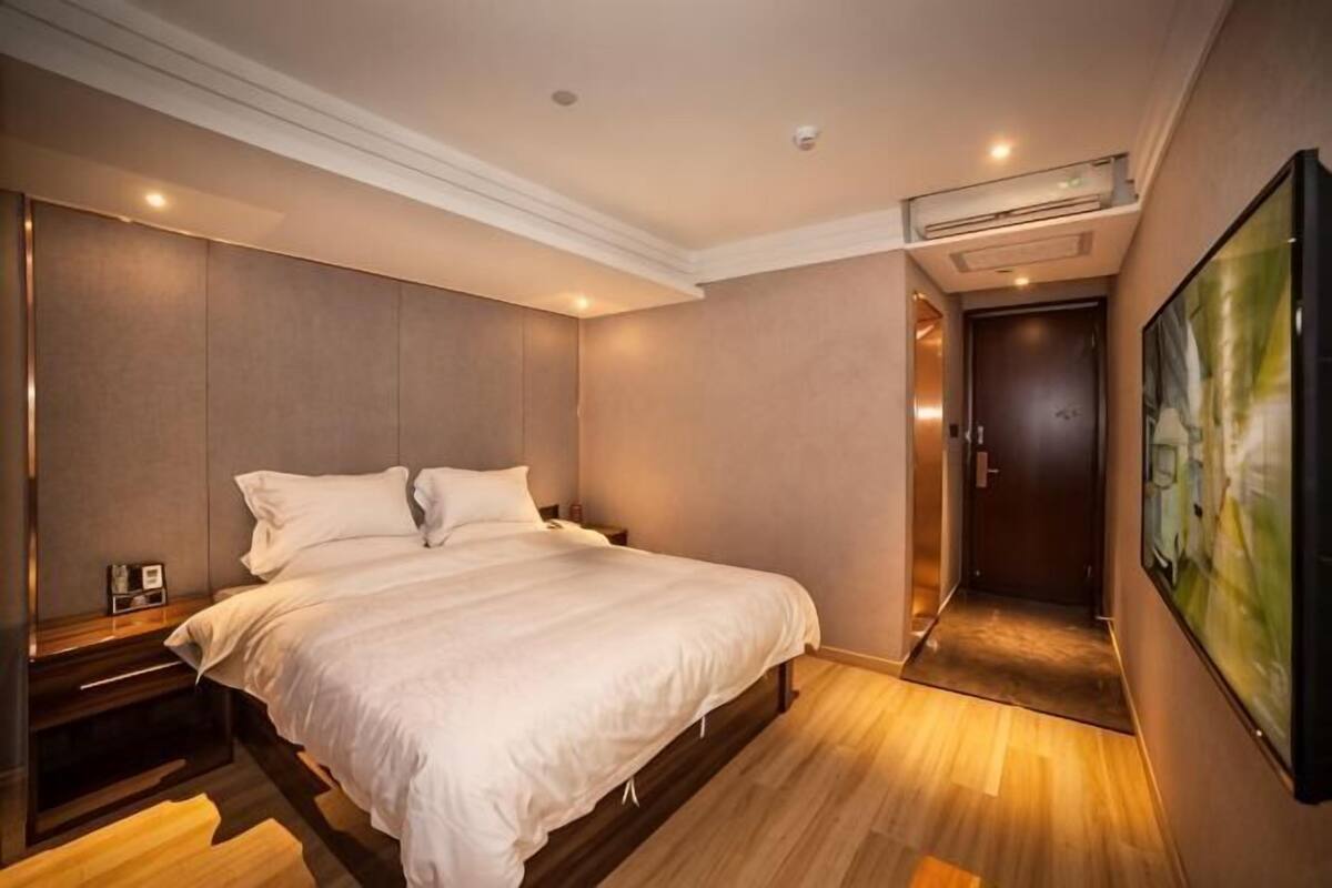 Una habitación de hotel con cama, mesita de noche, una obra de arte en la pared y una puerta que da a otra habitación.