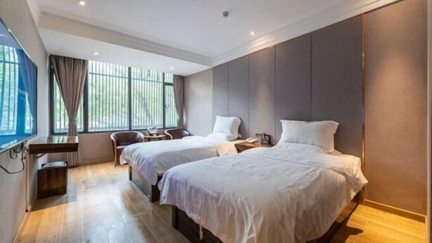 Ein Hotelzimmer mit zwei Betten, einem Schreibtisch, einem Stuhl und einem großen Fenster mit Vorhängen.