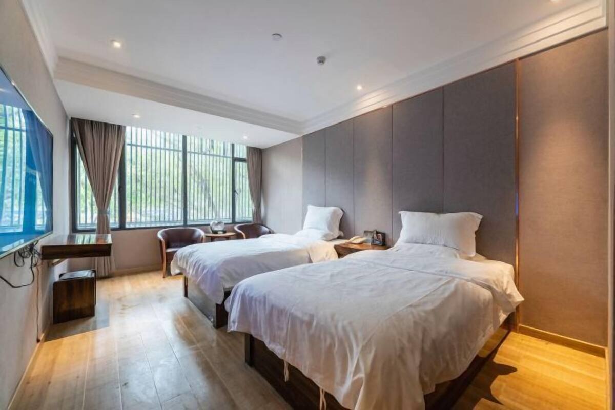 Habitación de hotel con dos camas, un escritorio, una silla y un ventanal con cortinas.
