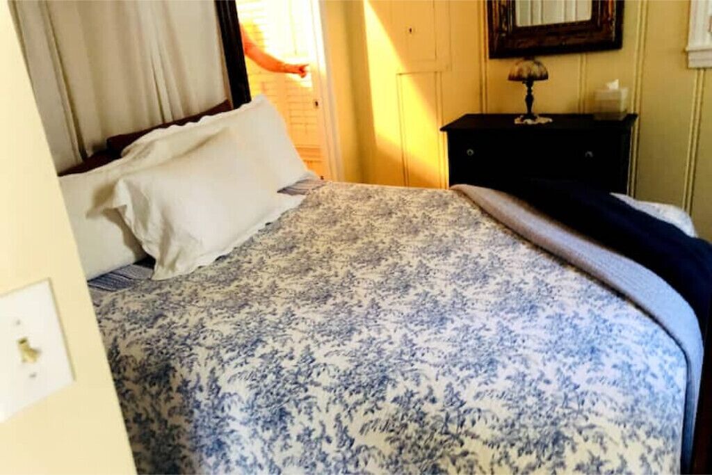 Un dormitori amb un llit, una tauleta de nit, una làmpada i un mirall a la paret.
