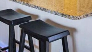 Une cuisine avec des meubles blancs, un plan de travail en granit et deux tabourets de bar noirs.