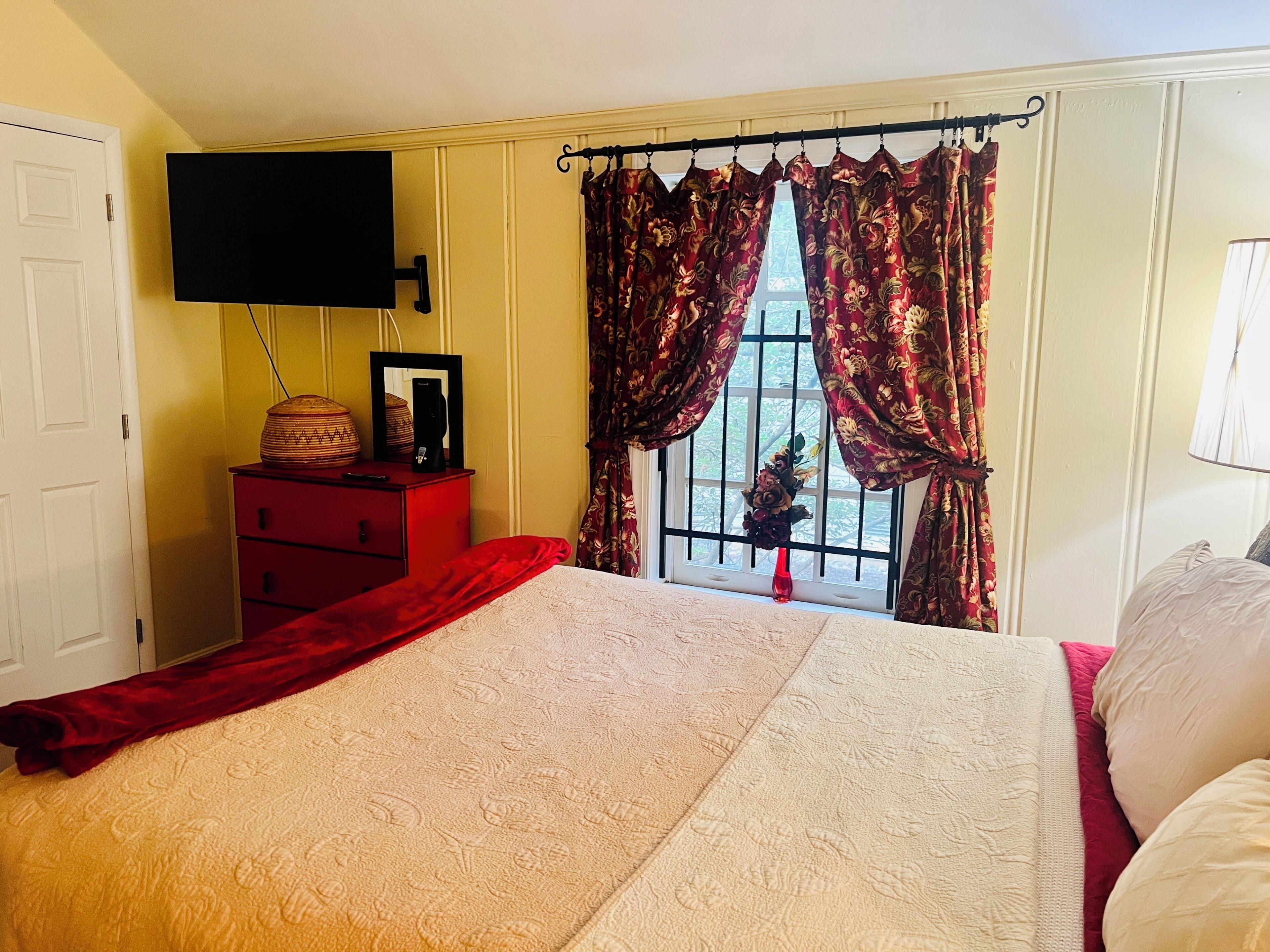 A bedroom with a bed, a dresser, a flat-screen TV, and a window with curtains.