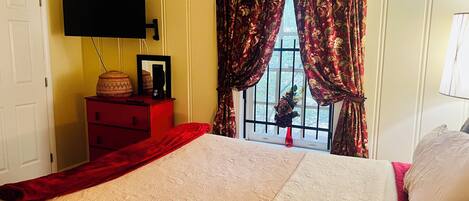 A bedroom with a bed, a dresser, a flat-screen TV, and a window with curtains.