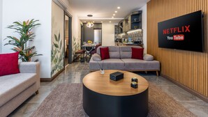 Un saló modern amb un televisor de pantalla plana que mostra 'NETFLIX YouTube', un sofà gris, una taula de centre i una zona de menjador al fons.