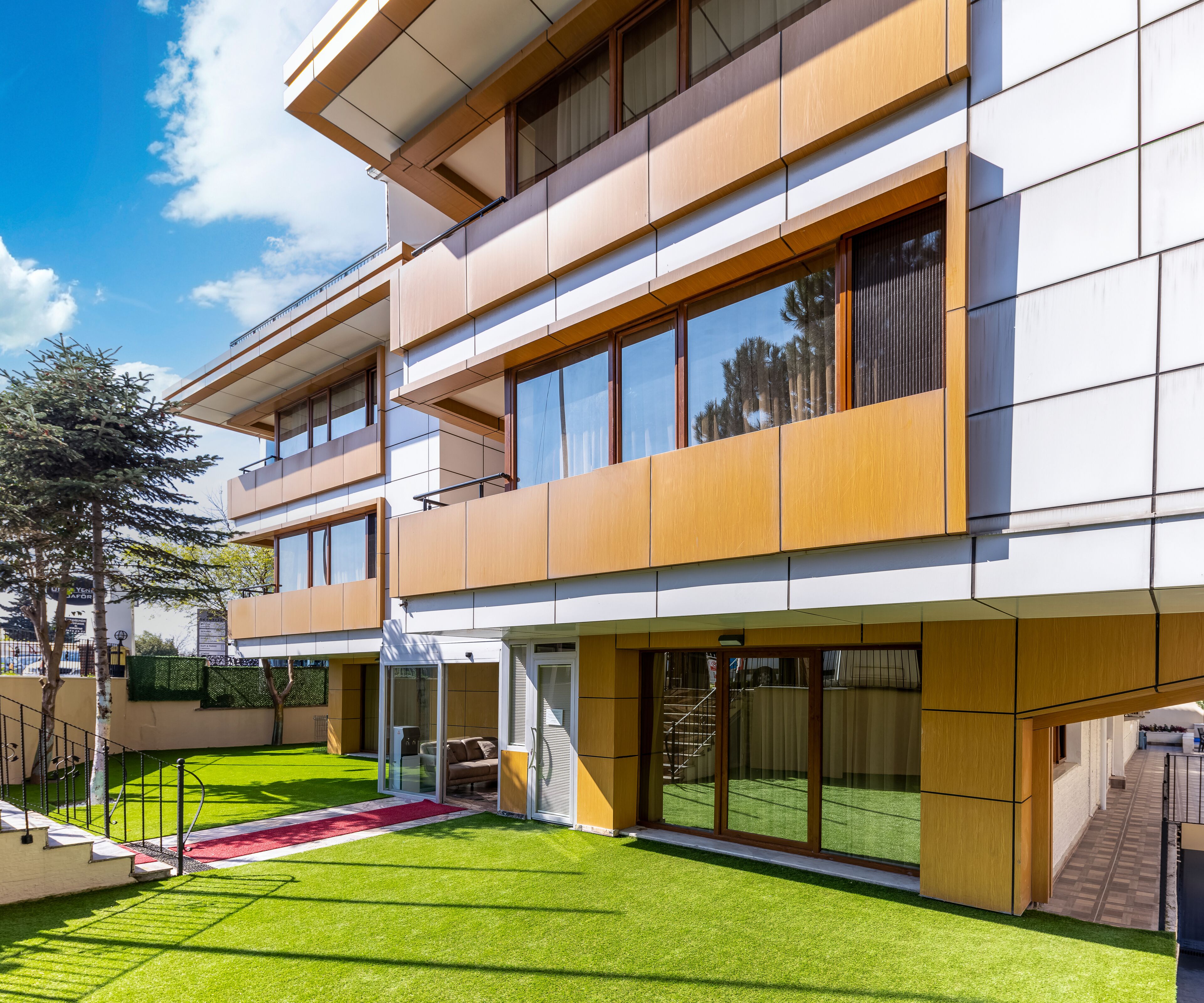 A modern multi-story building with a flat roof, large windows, and a well-maintained lawn.