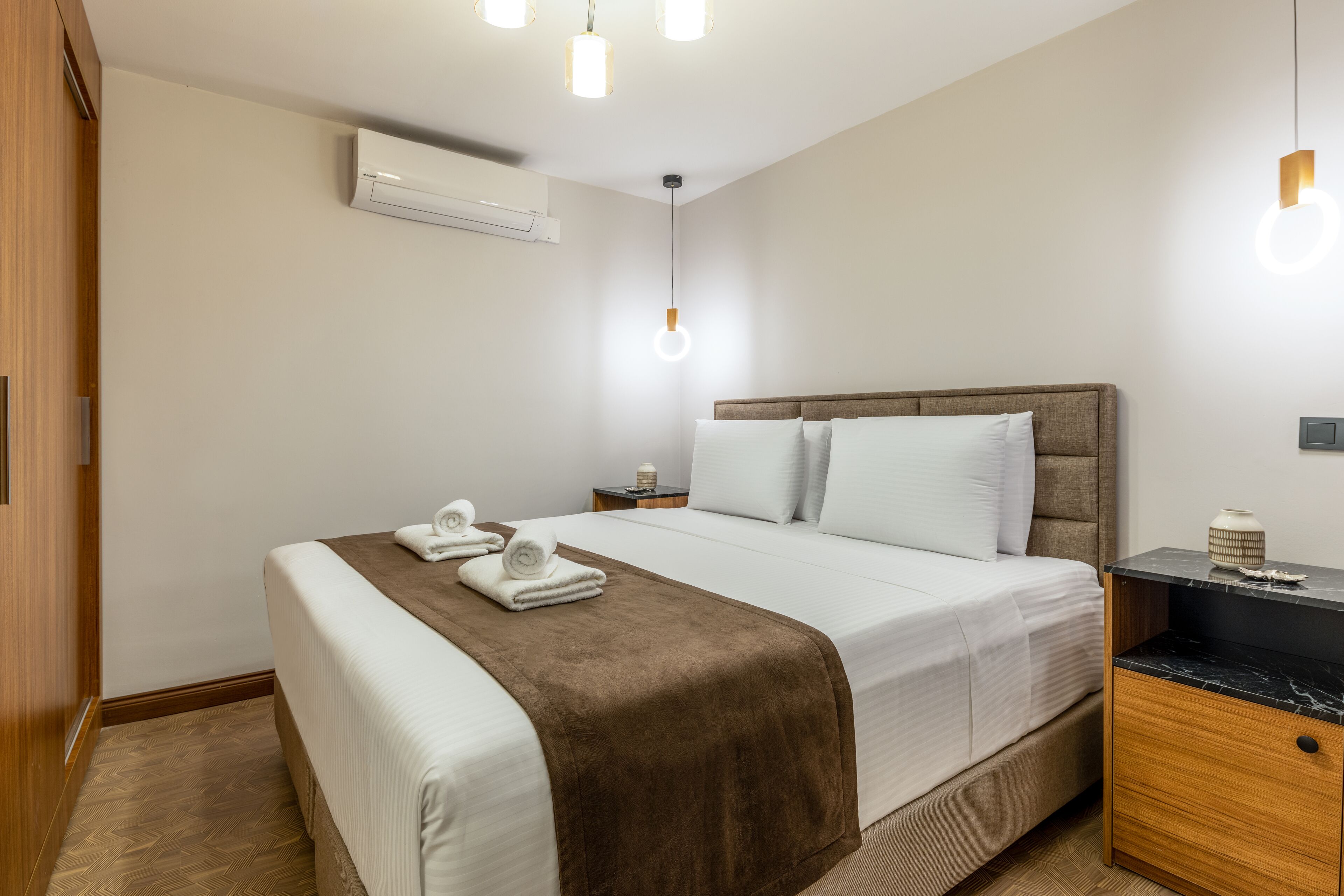 Quarto de hotel com cama, mesa de cabeceira, guarda-roupa de madeira e ar condicionado.