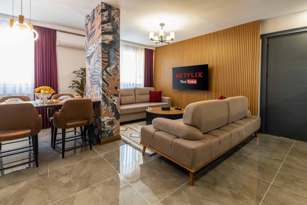 A modern living room with a sofa, dining table, chairs, and a TV displaying Netflix and YouTube logos.