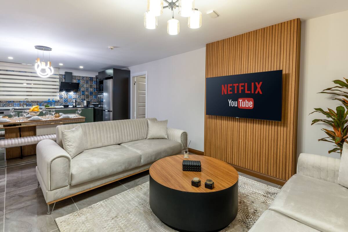 A modern living room with a sofa, coffee table, and a TV mounted on a wooden wall displaying 'NETFLIX YouTube'.