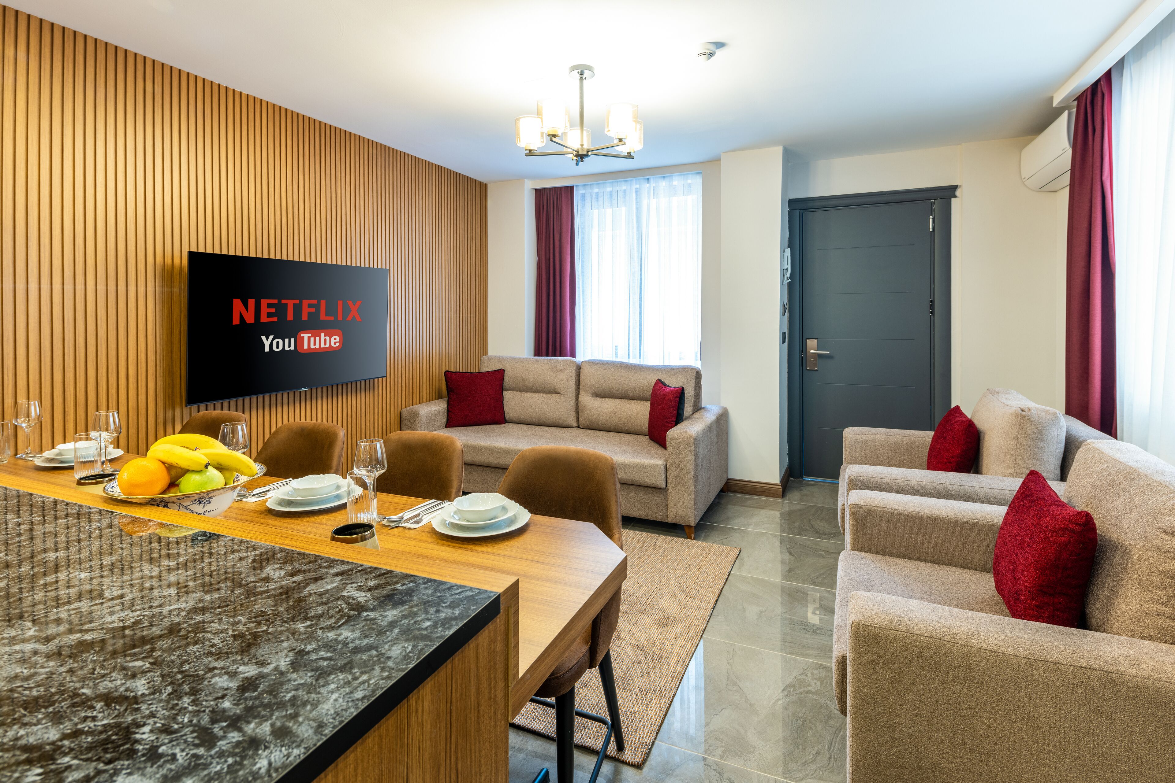 Ein modernes Wohnzimmer mit Fernseher, der 'NETFLIX YouTube' anzeigt, einem Essbereich mit Obstschale und einer Sofagarnitur.