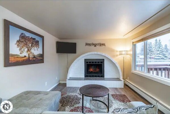 Cozy living room with a fireplace, TV, and large window offering a view of the surrounding landscape.