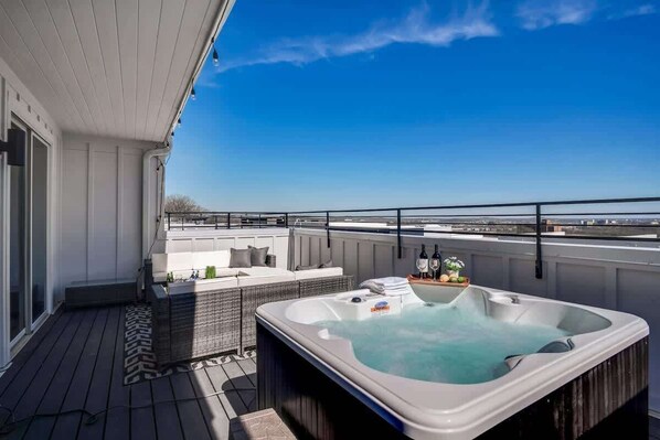 A rooftop deck with a hot tub, outdoor seating, and a view of the city skyline.