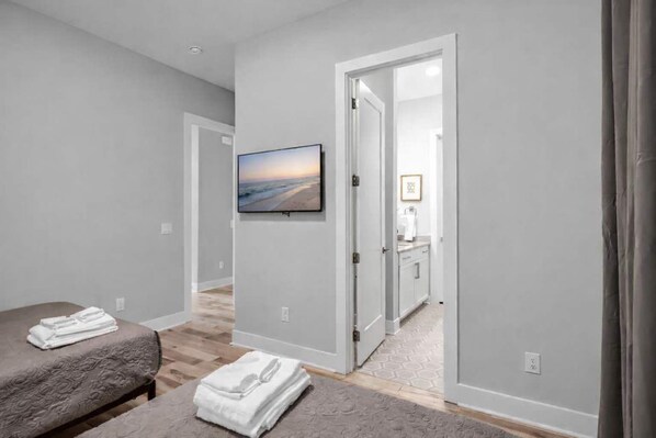 A bedroom with a bed, a bedside table, a folded towel, a painting, and a bathroom visible through an open door.