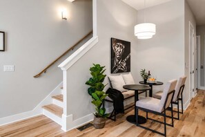Un intérieur moderne avec un escalier, un coin repas comprenant une table et des chaises, une plante en pot et une œuvre d’art accrochée au mur.