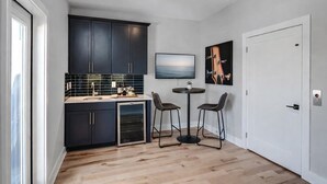 A modern kitchen with dark cabinets, a built-in oven, and a small dining area with two chairs and a table. - Skyline Hot Tub Retreat • Walk to Honky Tonks (Nashville)