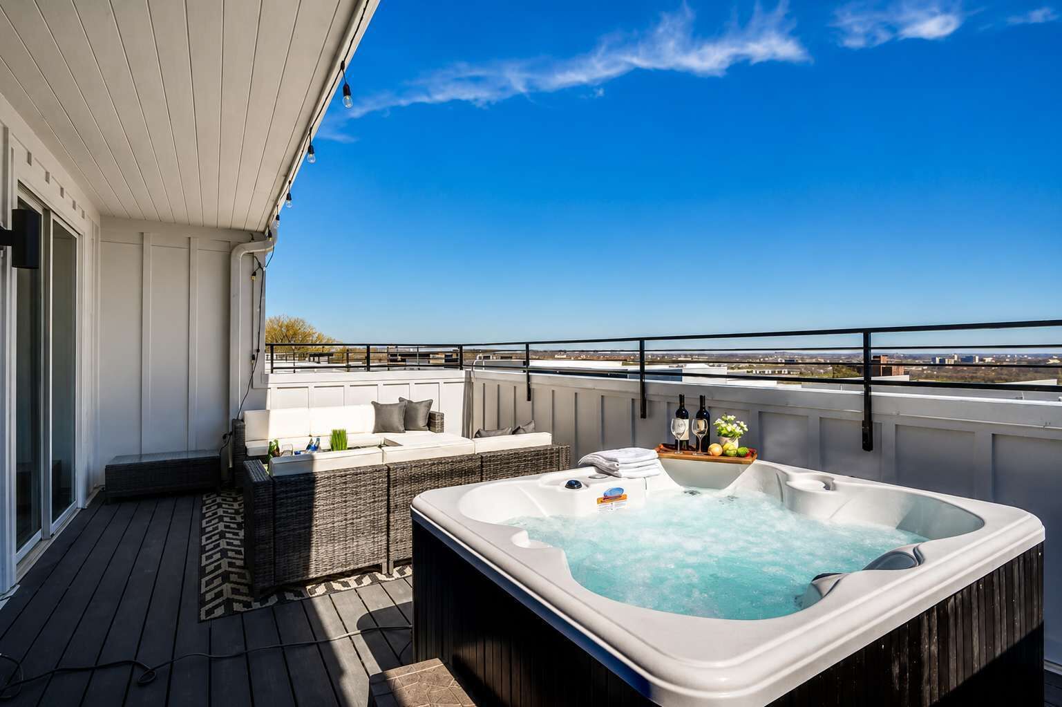 A rooftop terrace with a hot tub, seating area, and a view of the cityscape.