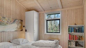 Un dormitori amb un llit, una biblioteca, una finestra amb vista a arbres i un quadre a la paret.