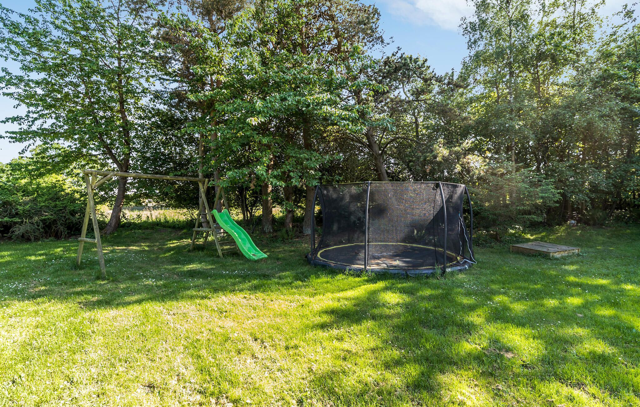 A trampoline with a safety net in a grassy outdoor area with trees.
