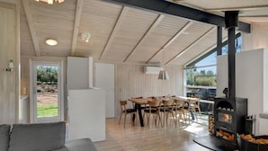 Un saló modern amb un sofà, una zona de menjador amb una taula i cadires, i una estufa de llenya.